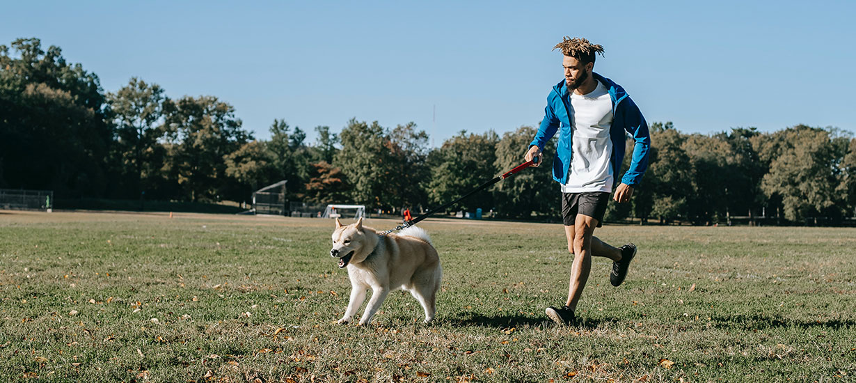 Man running in a soccer field with dog on leash
